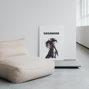 May include: A beige bean bag chair with a white poster behind it that says "Vagabond" in black text. The poster features a black and white illustration of a person with long hair.