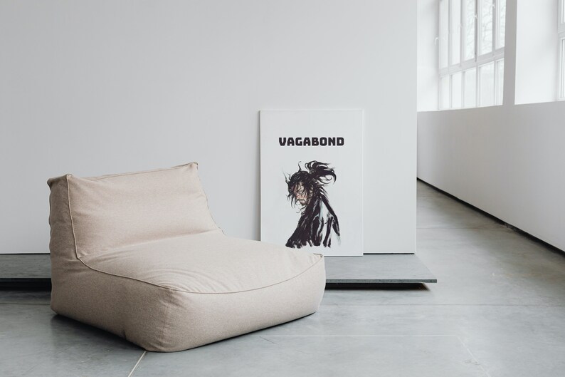 May include: A beige bean bag chair with a white poster behind it that says "Vagabond" in black text. The poster features a black and white illustration of a person with long hair.