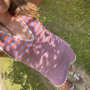 May include: A handmade crochet dress featuring alternating stripes of orange and lavender. The dress has a halter neckline and a scalloped edge. The dress is worn with brown sneakers.