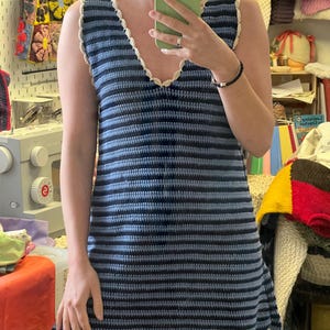 May include: A sleeveless, blue and navy striped crochet dress with a V-neckline and scalloped trim. The dress is handmade and appears to be a mini dress. The trim is a cream color.