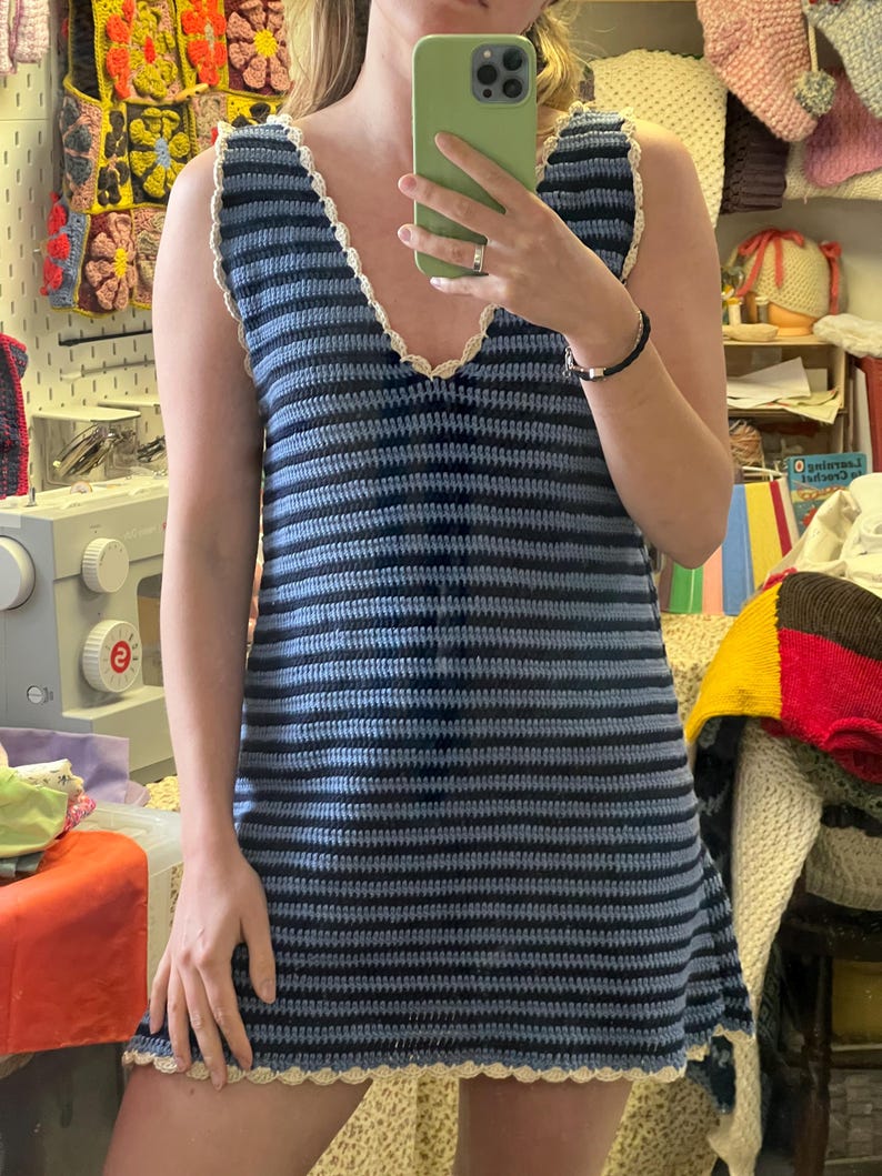 May include: A sleeveless, blue and navy striped crochet dress with a V-neckline and scalloped trim. The dress is handmade and appears to be a mini dress. The trim is a cream color.