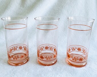 May include: Three clear glass tumblers with a pink floral design and a gold rim.