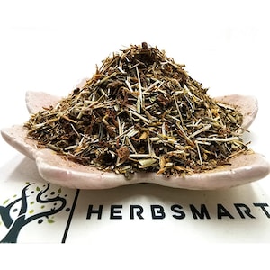 May include: A pile of dried herbs in a light pink ceramic dish. The herbs are a mix of light brown, green, and yellow.
