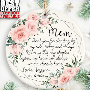 May include: White ceramic ornament with a pink floral design and the text "Mom thank you for standing by my side, today and always. Ever as this new chapter begins, my heart will always remain close to home. Love, Jessica 06.08.2024"