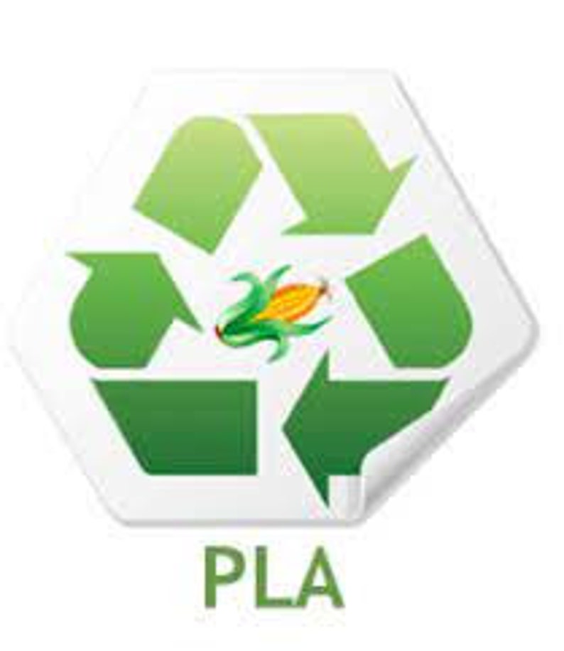 May include: A white, hexagonal sticker featuring a green recycling symbol with a corn stalk in the center. The word "PLA" is printed in green below the symbol. The sticker has a slight curve on the bottom right corner.