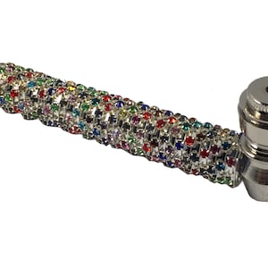 May include: A silver smoking pipe with a colorful rhinestone design. The pipe has a round bowl and a long, thin stem.