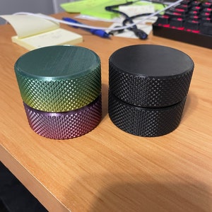 May include: Two cylindrical objects with textured surfaces. One stack features a gradient of green, yellow, and purple. The other stack is solid black. Both sets are on a wooden surface.