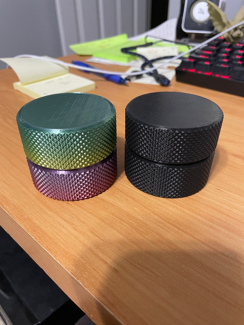 May include: Two cylindrical objects with textured surfaces. One stack features a gradient of green, yellow, and purple. The other stack is solid black. Both sets are on a wooden surface.