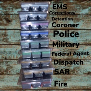 Könnte beinhalten: Ein Stapel von acht Wachs-Schmelzen in durchsichtigen Plastikbehältern. Jeder Behälter enthält drei einzelne Wachs-Schmelzen. Die Wachs-Schmelzen sind in verschiedenen Grautönen, Blau-, Grün- und Violetttönen. Der Text auf der rechten Seite des Bildes lautet: "EMS Corrections/Detention Coroner Police Military Federal Agent Dispatch SAR Fire".