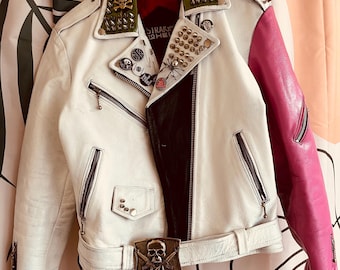May include: White leather motorcycle jacket with a black and pink color block design. The jacket has a green and black studded collar, a skull buckle, and a variety of metal studs and pins.