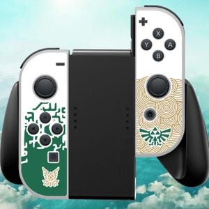 May include: A black game controller grip featuring two white detachable controllers. The left controller has a green graphic with a gold emblem, while the right controller displays a gold circular pattern and a green triforce-style symbol.