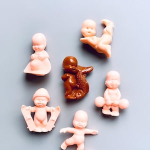Könnte beinhalten: Eine Sammlung von sieben kleinen Plastikfiguren von Babys, die verschiedene Aktivitäten ausführen. Die Figuren sind in Rosatönen und Braun gehalten, wobei eine Figur ein Paar Hanteln hält, eine andere Skateboard fährt und eine andere Ski hält.