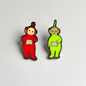 May include: Two enamel pins featuring characters from the children's television show Teletubbies. The pin on the left is red and the pin on the right is green.