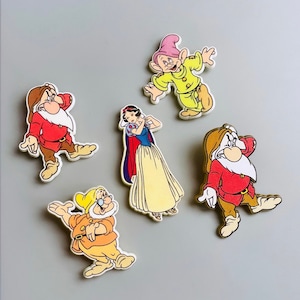 Könnte beinhalten: Fünf bunte Comic-Magnete mit Figuren aus dem Märchen Schneewittchen und die sieben Zwerge. Die Figuren sind Schneewittchen, Doc, Grumpy, Happy und Sneezy.