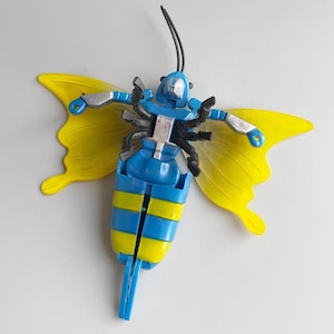 Pode incluir: Uma borboleta de brinquedo de plástico azul e amarelo com detalhes pretos. As asas são amarelas e o corpo é azul com listras amarelas.