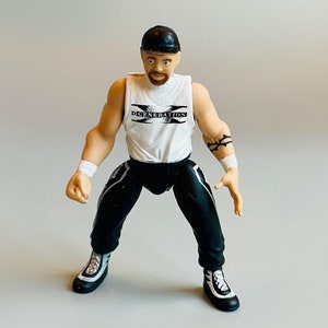 May include: A black and white action figure of a wrestler wearing a white tank top with the text "D-Generation X" on it. The figure is wearing black trousers and black and white shoes.