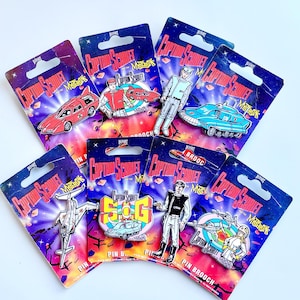 May include: A set of eight Captain Scarlet and the Mysterons enamel pins. The pins feature various characters and vehicles from the classic British science fiction television series. The pins are packaged on colourful cards with the show's logo and title.