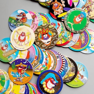 Könnte beinhalten: Eine Sammlung bunter Pogs mit Cartoon-Charakteren und verschiedenen Designs. Die Pogs sind rund und zeigen Bilder von lächelnden Kreaturen, Sportarten und anderen Grafiken. Einige Pogs tragen den Text "100% Authentic" und "TM & © 1995 WPF".