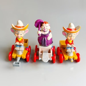 Peut inclure: Trois figurines de jouets vintage représentant des souris de dessins animés sur de petits wagons. Deux souris portent des chapeaux de cow-boy et des chemises rouges, tandis que la troisième souris est vêtue d'une robe violette et tient un parapluie violet. Les wagons sont jaunes avec des roues rouges.