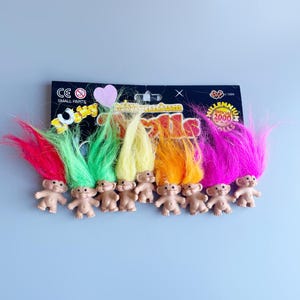 May include: A set of eight mini troll dolls with colorful hair. The trolls are arranged in a row on a black and white card with the text "Millennium Official 2000 Trolls".