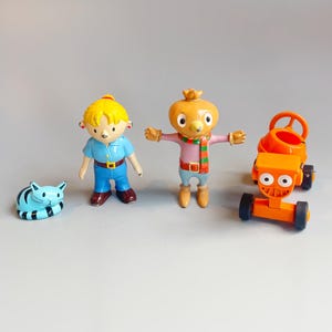 May include: A set of colourful toy figures. It includes a blue and black striped cat, a girl in a blue shirt and trousers, a character with an orange head and a striped scarf, and an orange toy cement mixer.