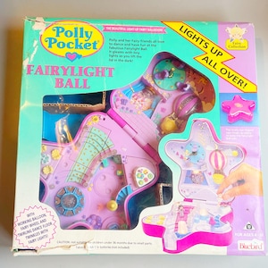 May include: A vintage Polly Pocket Fairylight Ball playset in its original box. The box is teal, pink, and purple, with the words "Polly Pocket" and "Fairylight Ball" displayed. The playset features a star-shaped design with a working balloon, fairy wheel, and twirling dance floor.