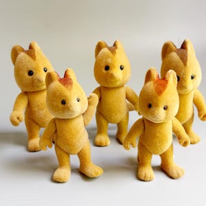 Può includere: Un set di cinque piccole statuette animali floccate con pelliccia giallo oro e una distinta macchia marrone rossiccio sulla fronte. Ogni figura presenta orecchie arrotondate, occhi a perla neri e una postura eretta con arti e code articolati.