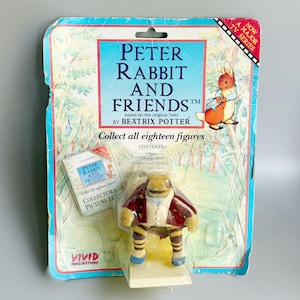 Op de afbeelding: Een Peter Rabbit and Friends Beatrix Potter verzamelfiguur in originele verpakking. De kaart bevat een illustratie van Peter Rabbit en tekst. Het figuurtje is een klein, antropomorf personage met een rood jasje en een gestreepte broek.
