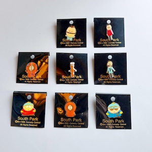 May include: Nine enamel pins featuring characters from the animated series "South Park." Each pin is attached to a black card with the show's logo and copyright information. The pins depict various characters in their signature outfits.