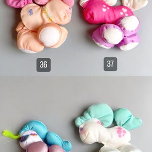 Pu&ograve; includere: Quattro personaggi di peluche dai colori pastello sono esposti su uno sfondo grigio. Ogni giocattolo ha un design unico, tra cui un unicorno, un pony e altre creature fantasy. I numeri 36, 37, 38 e 39 sono stampati sotto ogni giocattolo.