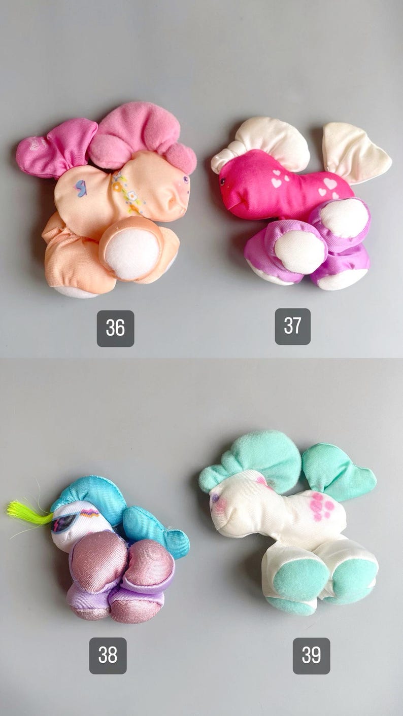 Pu&ograve; includere: Quattro personaggi di peluche dai colori pastello sono esposti su uno sfondo grigio. Ogni giocattolo ha un design unico, tra cui un unicorno, un pony e altre creature fantasy. I numeri 36, 37, 38 e 39 sono stampati sotto ogni giocattolo.