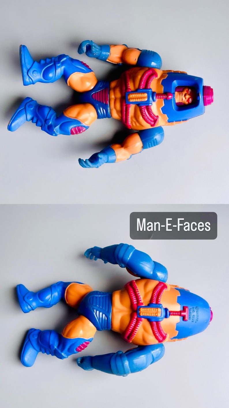 May include: A blue and orange action figure of Man-E-Faces from the Masters of the Universe toy line. The figure has a blue helmet with a face on it and a red and orange body. The figure is lying on its back with its arms and legs spread out.