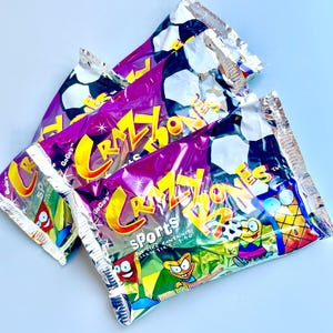 May include: Three unopened packages of Crazy Bones Sports trading cards. The packages are purple, silver, and blue with a cartoon character on the front. The text on the front of the packages reads "GoGo's Crazy Bones Sports".