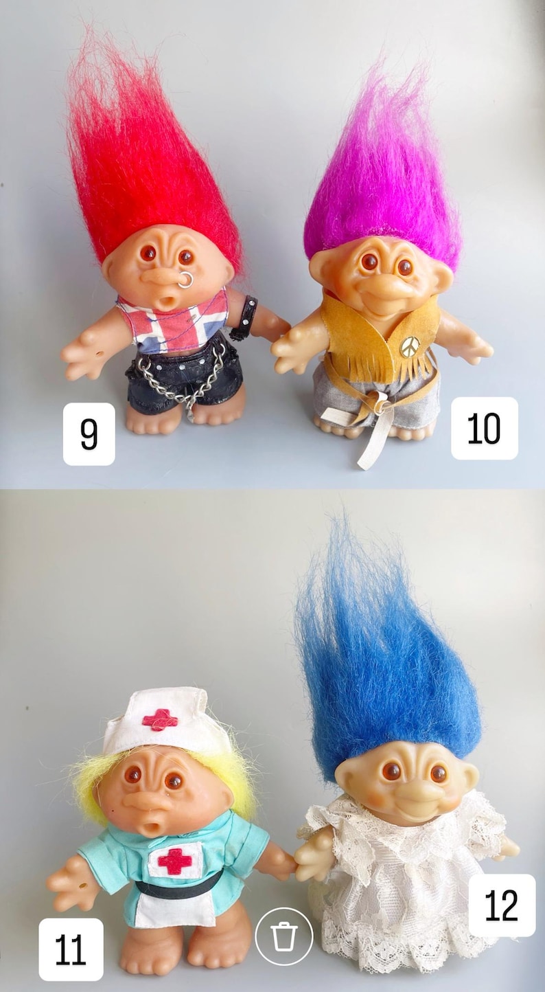 May include: Four troll dolls with different colored hair and outfits. The first doll has red hair and is wearing a black leather jacket with a Union Jack design, black pants, and a silver chain. The second doll has purple hair and is wearing a brown suede vest with fringe, gray pants, and a peace sign. The third doll has blonde hair and is wearing a blue nurse's uniform with a red cross. The fourth doll has blue hair and is wearing a white dress with lace.