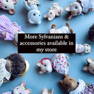 May include: A collection of Sylvanian Families animal figures, such as cats, hedgehogs, and rabbits, wearing tiny outfits. The toys are displayed on a pale blue background. The image includes the text: "More Sylvanians & accessories available in my store."