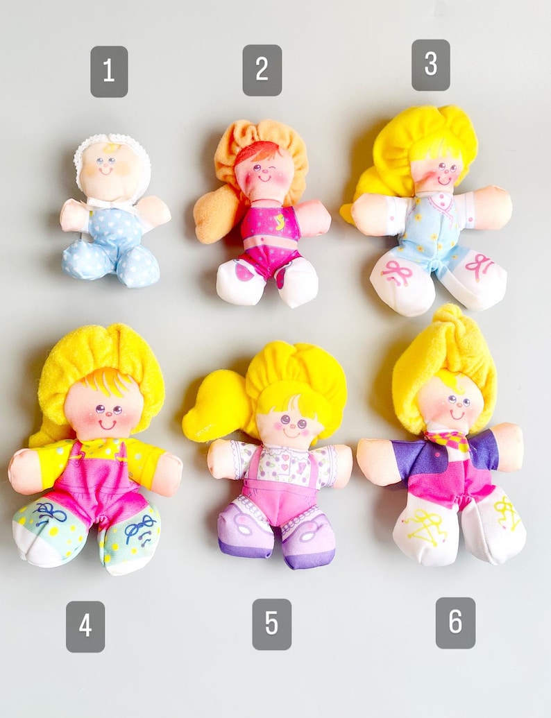 Pu&ograve; includere: Sei bambole di peluche vintage con volti dipinti e abiti colorati. Le bambole hanno capelli gialli o arancioni e indossano abiti nei toni del rosa, blu e viola. Ogni bambola ha un'espressione e un design unici.