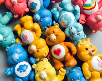 Puede incluir: Una colección de 12 figuras de Care Bear de colores. Cada oso tiene un diseño y un símbolo únicos en su vientre. Los osos son de plástico y están en buen estado.