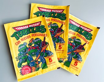 May include: Three Teenage Mutant Ninja Turtles trading cards with colourful illustrations of the characters and the text "Teenage Mutant Turtles" and "Con nuevos personajes". Each card features the text "Contiene 5 figuritas" and "Houstra Argentina".