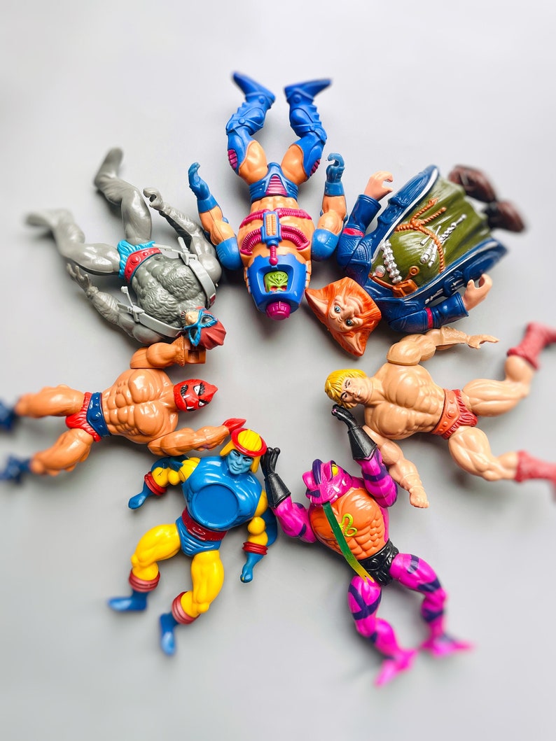 May include: A group of seven colorful action figures, including a blue and purple figure with a yellow chest, a yellow and blue figure with a red head, a red and yellow figure with a red head, a purple and orange figure with a green head, a gray figure with a red head, a blue and red figure with a blue head, and a blue and green figure with a brown head.
