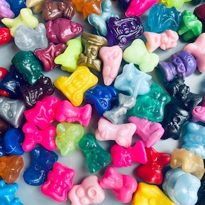 May include: A collection of colorful, small, plastic figurines in various shapes and designs. The figurines are arranged on a light gray surface.