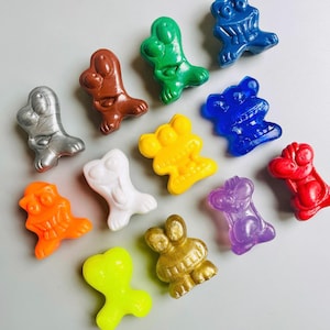 May include: A selection of brightly coloured, abstract figurines in shades such as silver, brown, green, blue, yellow, white, orange, gold, purple, red, and neon green. The figurines have a unique shape and are arranged on a light grey surface.