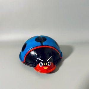 May include: A blue and black wind-up ladybug toy with red and yellow facial features. The ladybug has black dots on its back.