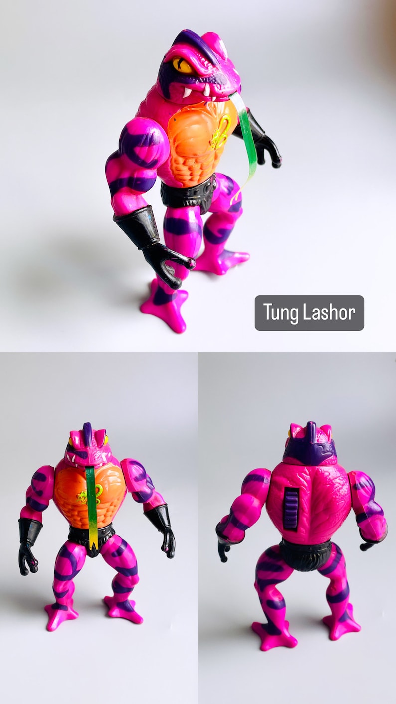 May include: A pink and purple action figure of Tung Lashor from the Masters of the Universe toy line. The figure has a frog-like head with a long tongue and a muscular body with a black belt. The figure is posed in a standing position with its arms outstretched.