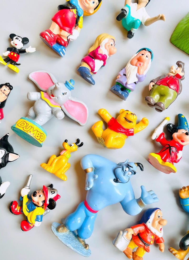 May include: A collection of vintage Disney character figurines, including Mickey Mouse, Winnie the Pooh, Dumbo, and Aladdin. The figurines are made of plastic and are painted in bright colors.