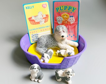Puede incluir: Un conjunto de figuras Puppy in My Pocket que incluye un perro pastor grande gris y blanco, dos cachorros más pequeños y dos cachorros en miniatura dentro de una cesta de plástico morada. Se incluyen dos tarjetas coleccionables, Kelly y Puppy in My Pocket.