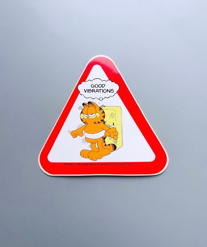 Puede incluir: Un cartel de advertencia triangular rojo con un gato naranja de dibujos animados, Garfield, en su interior. El cartel dice "GOOD VIBRATIONS" en una burbuja de pensamiento sobre la cabeza de Garfield. El cartel tambi&eacute;n incluye la informaci&oacute;n de copyright: "SP1064 &copy; 1978 United Feature Syndicate Inc. SPI Ltd (0532) 465471".