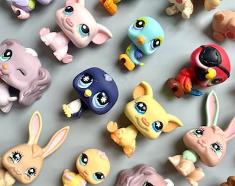 May include: A collection of colorful plastic toy animals, including a pink pig, a yellow chick, a blue bird, a brown bunny, a purple dog, a red bird, and a white dog. The toys are all small and have large eyes.