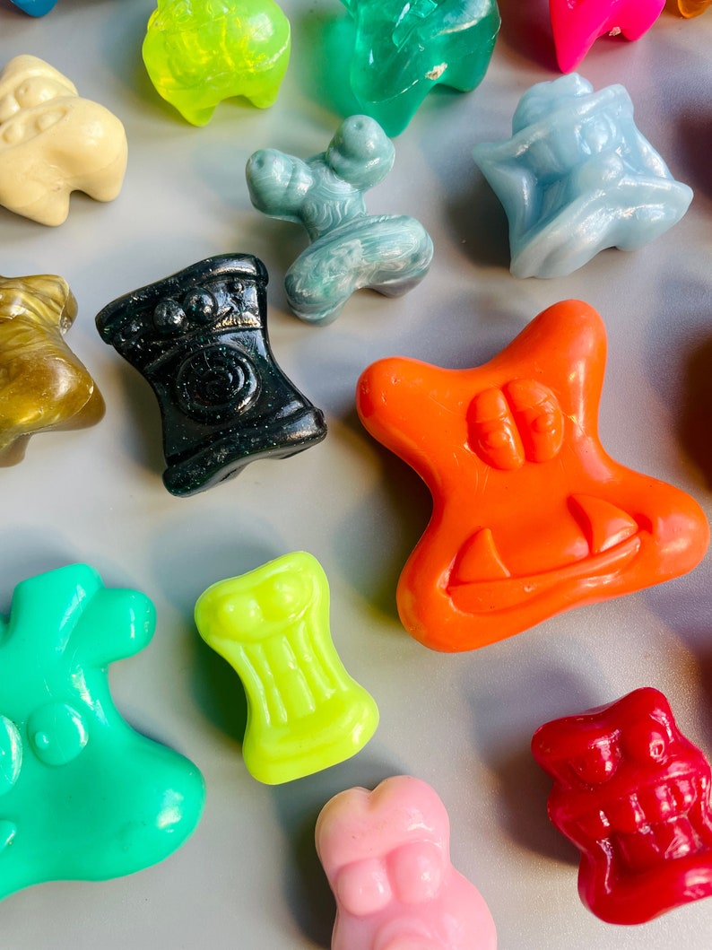May include: A collection of colorful, small, plastic toys in various shapes and designs. The toys are made of a smooth, glossy material and have a variety of colors, including green, blue, orange, red, pink, and black.