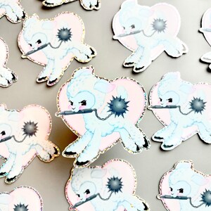 May include: A set of 10 pastel blue and pink glitter stickers featuring a cartoon lamb holding a spiked ball and a sword. Each sticker is shaped like a heart.