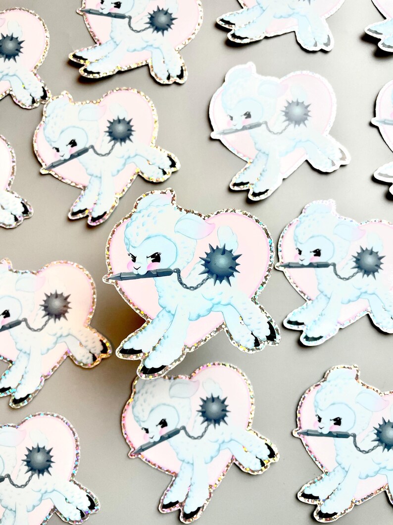 May include: A set of 10 pastel blue and pink glitter stickers featuring a cartoon lamb holding a spiked ball and a sword. Each sticker is shaped like a heart.